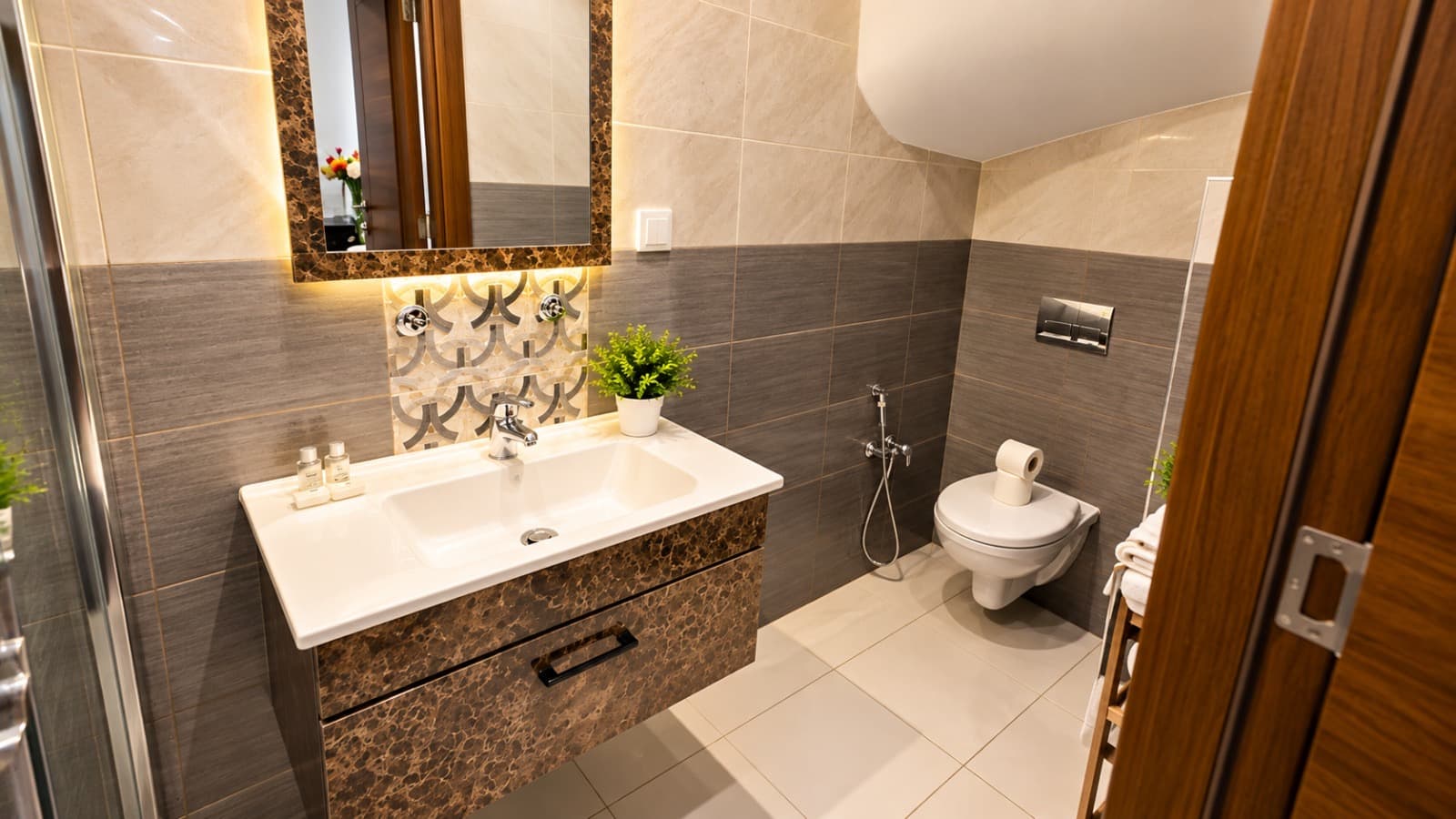 Salle de bain beige et grise avec meuble vasque façon marbre brun et miroir lumineux