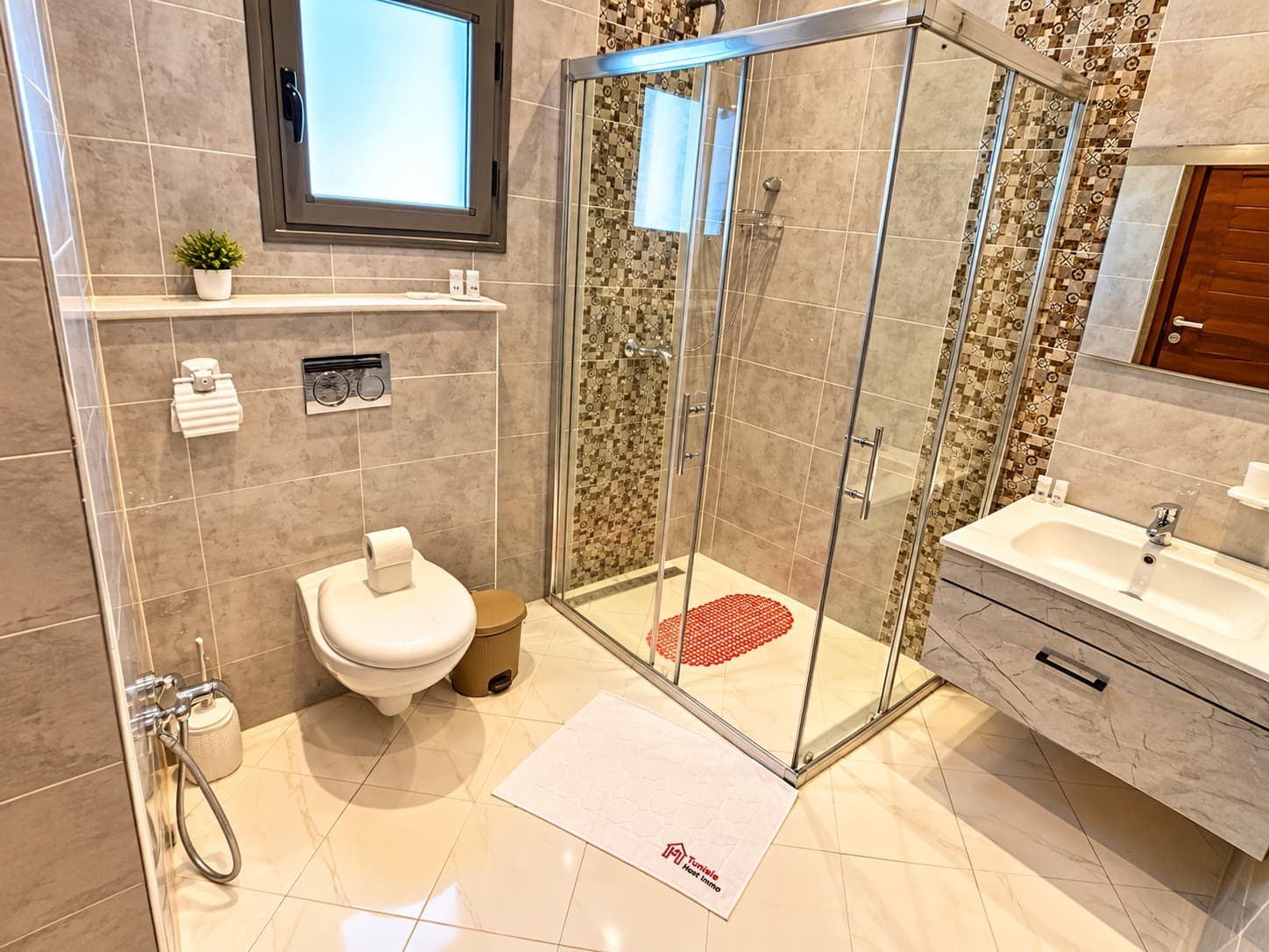 Salle de bain grise avec cabine de douche vitrée, vasque suspendue et carrelage à motifs